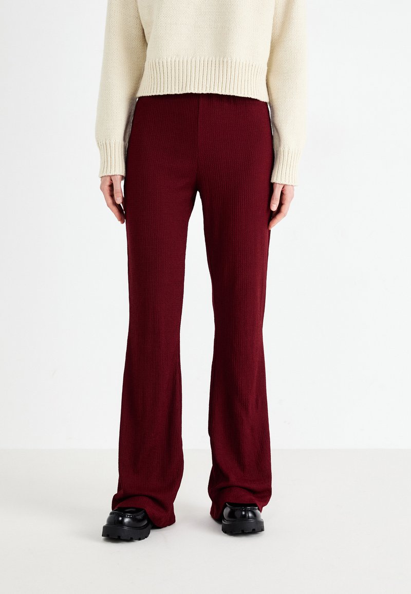 Pantaloni din tricot rib batut în burgund, evazați, realizati dintr-un tricot texturat. Asortați cu un pulover crem, cu o siluetă drept și talie elastică.