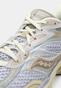 Γκρι και μπεζ αθλητικό παπούτσι με επάνω από δίχτυ, διαθέτοντας παχύ τζάκετ, επίπεδους κορδόνες και υφή σόλας με έντονο λογότυπο.