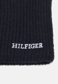 Sciarpa blu navale lavorata a maglia con texture a coste; presenta il logo ricamato "HILFIGER" in bianco nella parte inferiore.