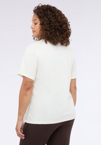 Camiseta de manga corta color crema con cuello redondo. Tejido suave con una textura lisa, corte relajado y detalles de costura sutiles en la parte posterior.