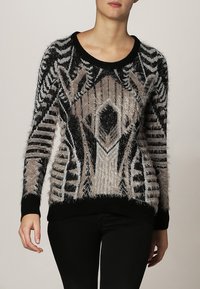 Maglione a motivo nero e beige con una consistenza morbida, scollo rotondo e maniche lunghe con orlo a coste. Design geometrico su tutta la superficie.