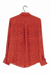 Chemise à imprimé serpent rouge en tissu léger. Elle possède des manches longues et un col avec un détail de pli à l'arrière. Suspendue à un crochet.