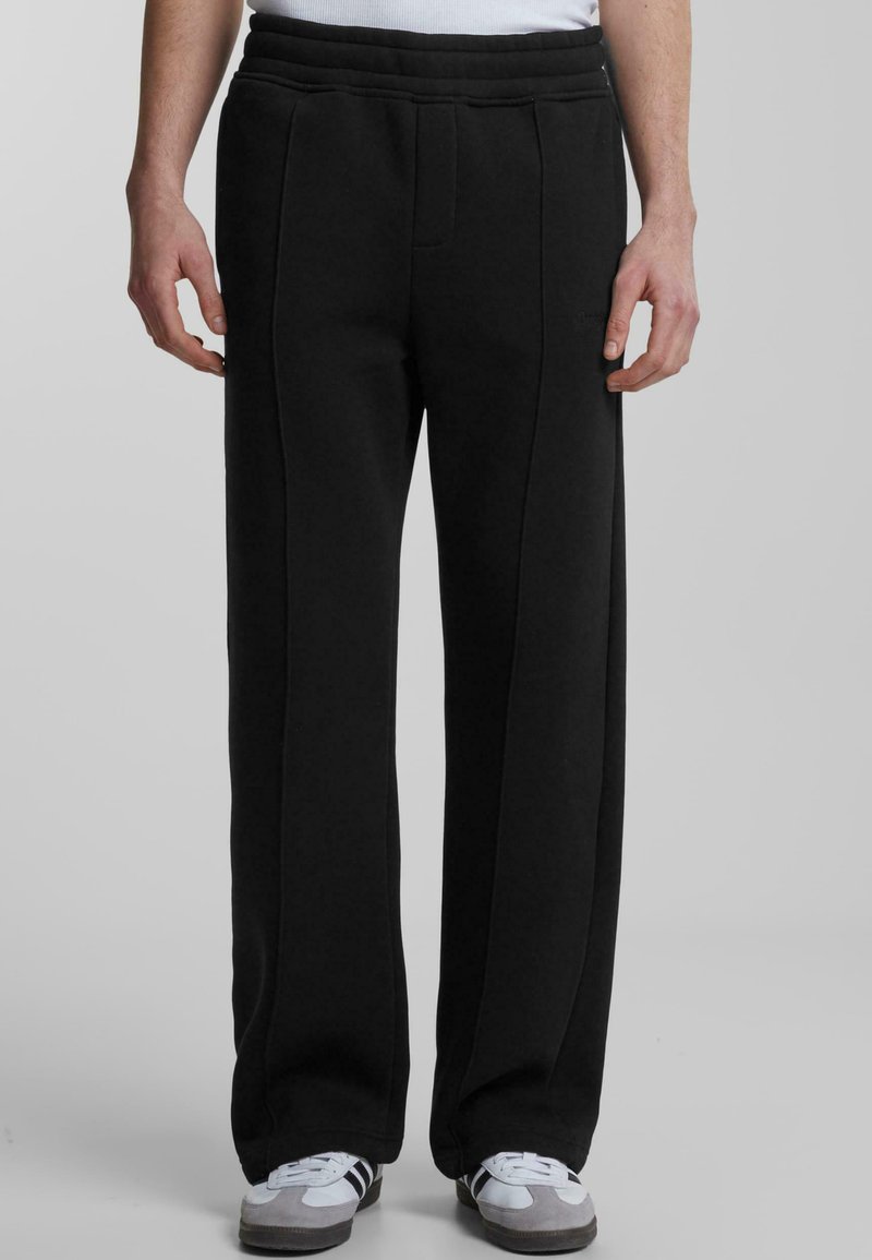 Black sweatpants with a flat waistband, two front seams, and a straight leg design. Material appears soft and textured.