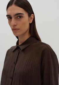 Brown button-up shirt with a textured fabric, featuring a collar and subtle sheen, showing the front part and shoulder of the garment.