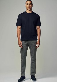 Sort bomulds crew-neck t-shirt parret med grå slim-fit bukser. Modellen har sorte sneakers på og står foran en neutral grå baggrund.