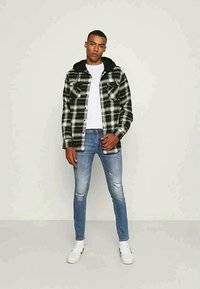 Camisa xadrez em preto e branco com capuz preto, combinada com jeans skinny desbotados em azul claro e ténis brancos.