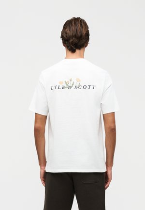 Άτομο που φαίνεται από πίσω φοράει λευκό κοντομάνικο μπλουζάκι με το κείμενο «LYLE & SCOTT» και γραφικά κίτρινου λουλουδιού στο πάνω μέρος της πλάτης.