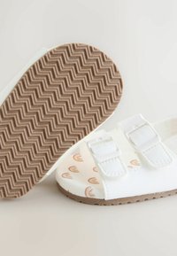 White sandals with two adjustable straps, patterned inner sole featuring rainbows, and a textured brown rubber outsole.