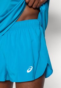 Τουρκουάζ αθλητικό σορτς με ελαστική μέση και λευκό λογότυπο. Το ύφασμα έχει ομαλή υφή με αεριζόμενο σχέδιο στο πλάι.