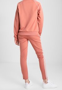 Pink athletic tracksuit featuring a crew neck sweatshirt and tapered pants with white side stripes. Made of soft, flexible material. White sneakers.