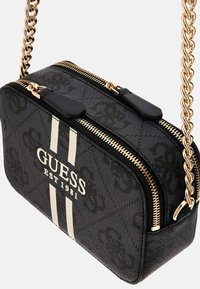 Black crossbody bag with textured finish, gold chain strap, dual zip closure, white stripes, and engraved brand logo.