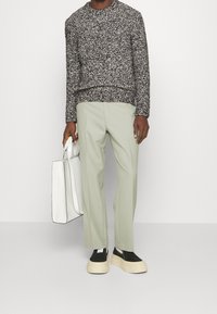 Suéter de punto en un patrón salpicado en blanco y negro, pantalones ajustados de color verde claro, zapatos negros tipo mocasín con una suela gruesa de crema y una bolsa tote blanca.