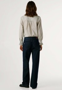 Vaqueros de mezclilla en azul oscuro con un corte recto, combinados con una blusa de cuadros clara con mangas largas y detalle fruncido en la parte trasera.