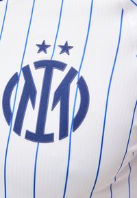 Logo bleu foncé de l'Inter Milan avec deux étoiles au-dessus, centré sur un maillot blanc avec des rayures verticales bleues.
