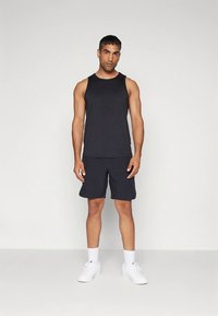 Czarny bezrękawnik i dopasowane szorty wykonane z gładkiej tkaniny. Dopełnieniem stroju są białe trampki. Prosty design i sportowe dopasowanie.