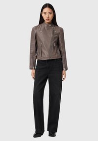 Braune Leder-Motorradjacke mit gerippten Schulterakzenten, Reißverschluss vorne und Taschen, kombiniert mit hoch taillierter schwarzer Jeans.