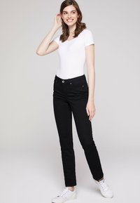 Vaqueros de mezclilla negros con un ajuste slim, que cuentan con bolsillos frontales, cierre con cremallera y un botón plateado. Combinados con una camiseta ajustada de manga corta blanca.