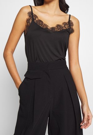 Czarna koszulka na ramiączkach wykonana z miękkiego materiału, z koronkową lamówką przy dekolcie i cienkimi ramiączkami, zestawiona z wysokim stanem spodniami o kroju tailored.
