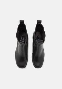 Paire de bottines en cuir noir avec languettes, bouts carrés et panneaux latéraux élastiques, vues de dessus sur fond blanc.