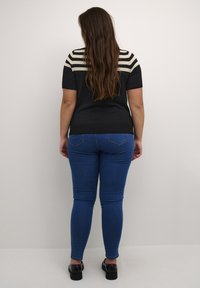 Black short-sleeve top with cream stripes on shoulders, paired with blue skinny jeans and black patent shoes. Smooth texture, fitted design.