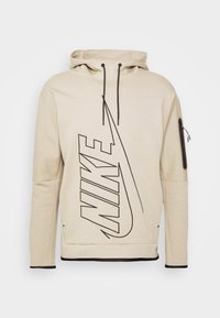 Beige Kapuzenpullover aus weichem Material mit großem schwarzem Nike-Logo, Kapuze mit Kordelzügen und einer Reißverschlusstasche an dem linken Ärmel.