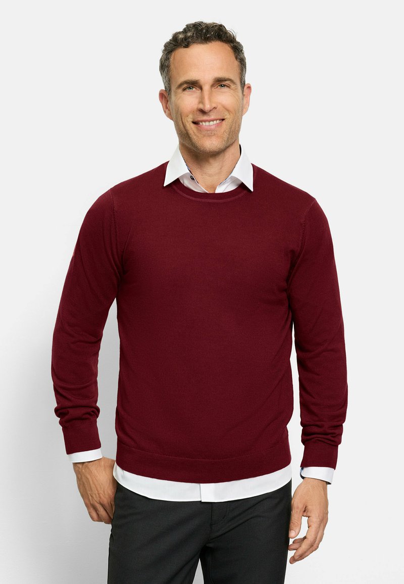 Burgunderfarbener Rundhalsausschnitt-Pullover aus weichem Strickmaterial, mit langen Ärmeln und taillierter Passform, über einem weißen Hemd mit Kragen getragen.