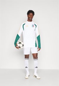 Valge jalgpallivarustus roheliste aktsentidega ja kuldsete triipudega, millel on Italia embleem. Hoidmas musta ja valget jalgpall.