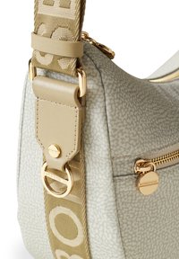 Beige patterned shoulder bag with a textured surface, gold hardware, and a wide strap featuring a logo design. Zippered pocket detail.