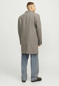 Palton gri din lână cu guler în formă de V, mâneci lungi și croi drept. Asortat cu blugi din denim generoși și pantofi negri.