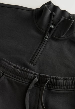 Schwarzer Sweatshirt mit halbem Reißverschluss und texturiertem Stoff; verfügt über einen elastischen Bund mit Kordelzug und Taschen-Detail.