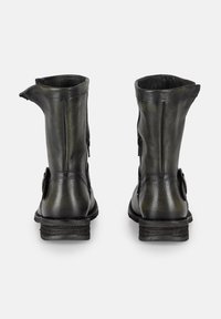 Botas de cuero negras a la altura del tobillo con un acabado ligeramente desgastado, forma afilada, cierre de cremallera y detalles decorativos de correas en los laterales.