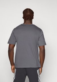 T-shirt gris à manches courtes avec un col rond, fabriqué en tissu doux. Design uni avec des détails de couture visibles au niveau des épaules.