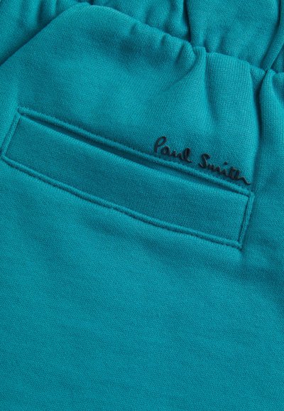 Tyrkysový materiál s texturovaným povrchem, který má prošitou kapsu a černé logo "Paul Smith" na boku.