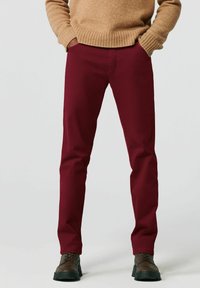 Bordeauxrode katoenen broek met een rechte pijp, voorzien van een gladde textuur en voorzakken, gedragen met bruine veterlaarzen.