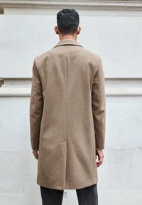 Cappotto di lana marrone con taglio dritto, colletto a revers e texture sottile; presenta uno spacco posteriore singolo e maniche lunghe.