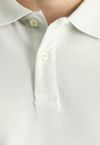 Polo bianca realizzata in tessuto a costine, con colletto classico e due bottoni al collo. Texture liscia con una leggera lucentezza.