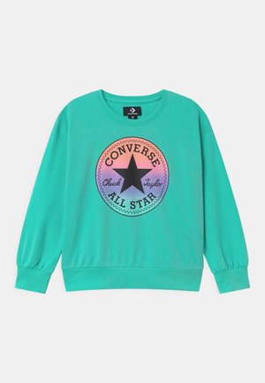 Sudadera turquesa con mangas largas, puños acanalados y cuello redondo. Presenta un gráfico circular multicolor con una estrella y texto.
