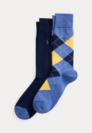 Une paire de chaussettes unies bleu foncé et une paire de chaussettes à motif losanges bleu, jaune et bleu foncé côte à côte.
