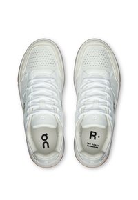 White sneakers with perforated detailing, flat laces, and rubber soles. Features branding on the tongue and insoles. Smooth leather texture.