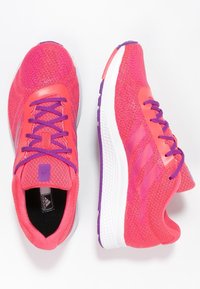 Baskets de sport roses avec une tige en maille, des lacets violets et une semelle texturée blanche. Elles disposent de trois rayures sur le côté et d'un collier rembourré pour plus de confort.