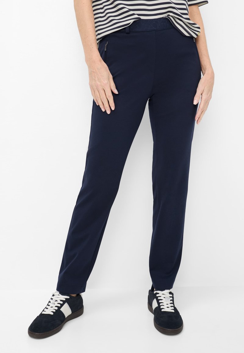 Persona che indossa pantaloni blu navy, scarpe da ginnastica nere e bianche e una maglietta a righe blu navy e bianca su uno sfondo bianco.
