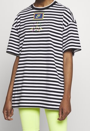 Zwart-wit gestreept T-shirt met korte mouwen, met Nike-logo en kleurrijk vredessymbool, gedragen met neongele shorts door een persoon.