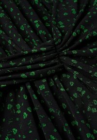 Tissu noir avec un motif marbré vert, présentant une texture douce et un détail froncé au centre. Convient pour une tenue décontractée ou formelle.