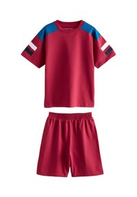 T-shirt rouge en coton à manches courtes avec des accents d'épaule bleus et des rayures noires, blanches et rouges. Associée à un short à taille élastique rouge.