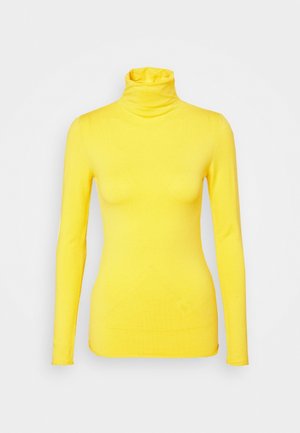 Pull jaune à col roulé à manches longues avec une silhouette ajustée sur fond gris clair uni.