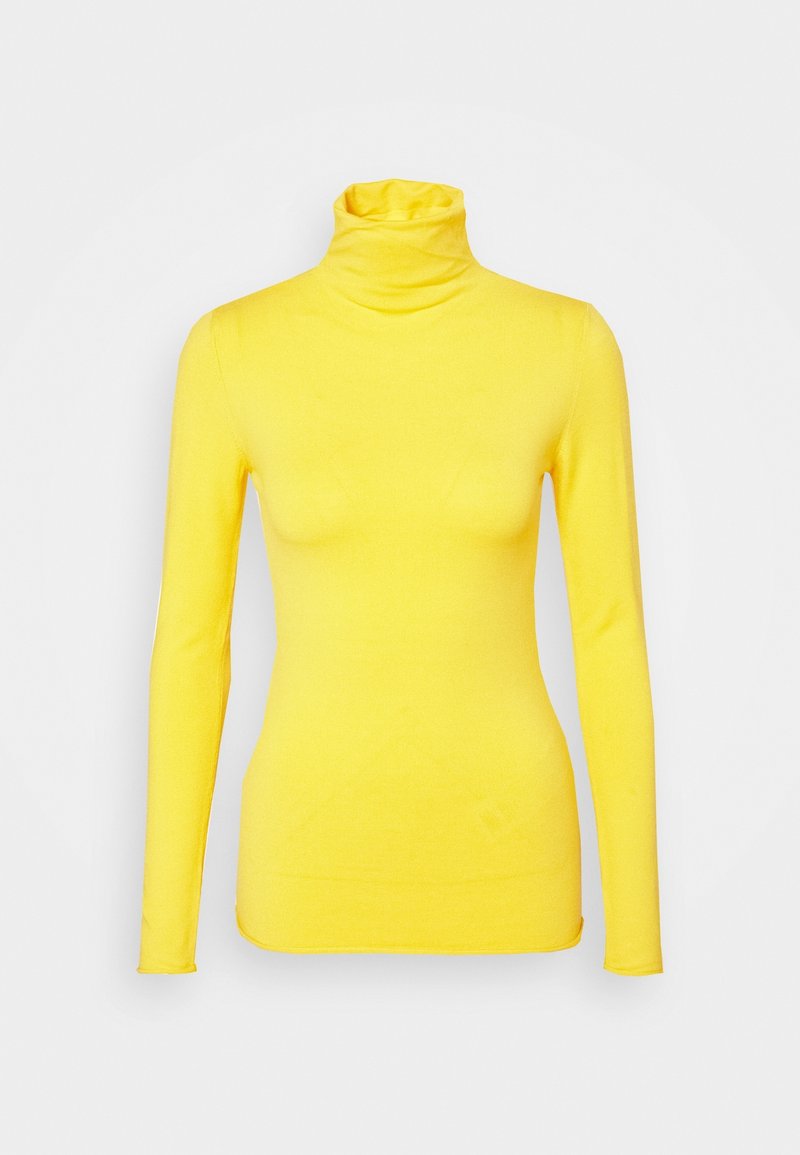 Pull jaune à col roulé à manches longues avec une silhouette ajustée sur fond gris clair uni.