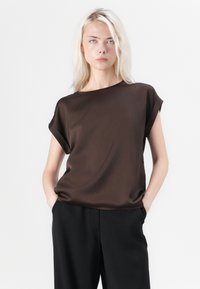 Brown satin blouse with a loose fit, short rolled sleeves, and a round neckline, paired with black wide-leg trousers. Smooth texture.