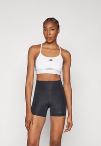 Sujeta blanca con acentos y logo en negro, combinada con pantalones cortos negros de cintura alta que presentan un logo sutil, textura suave y diseño ajustado.