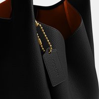 Zwarte handtas van gekorreld leer met een gladde bruine binnenvoering en een hangend leren label bevestigd aan een gouden kogelkettinkje.