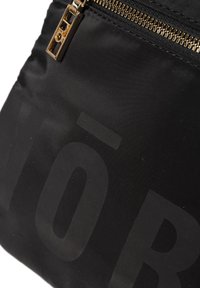 Zwarte stoffen tas met een gouden rits en reliëfletters. Glad van structuur met een matte afwerking, die een minimalistisch ontwerp benadrukt.